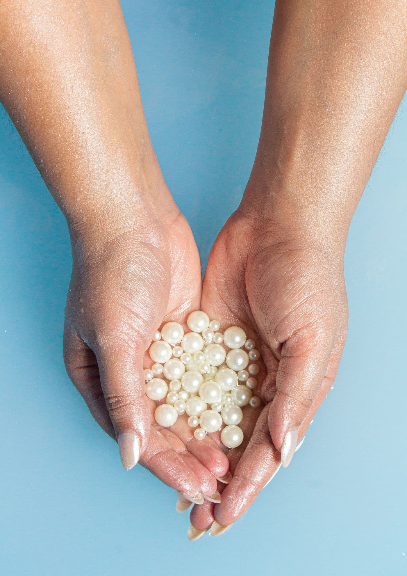 Two cupped hands comparing a pile of loose pearls of varying sizes