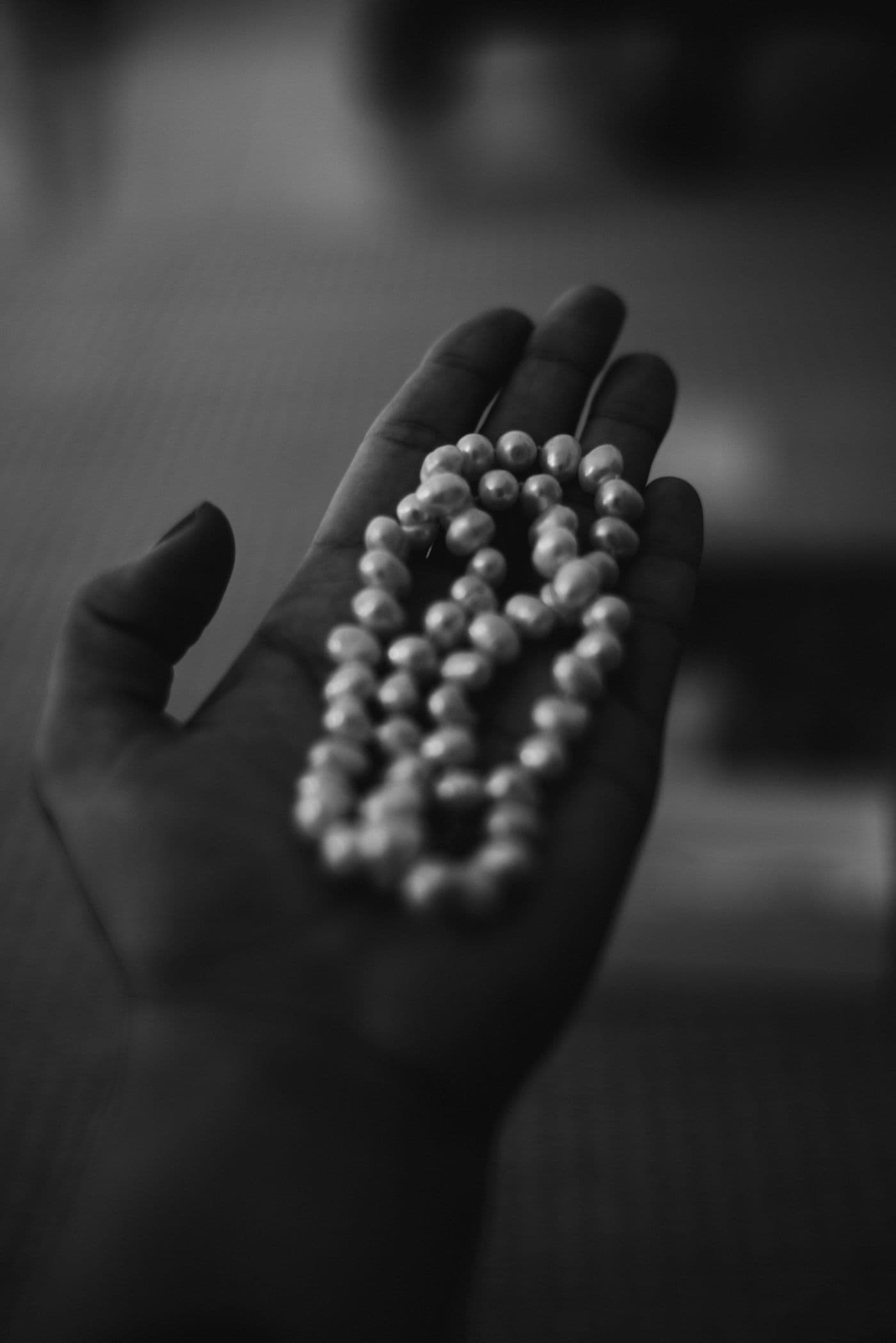 A hand cradling a strand of loose pearls, examined in low light