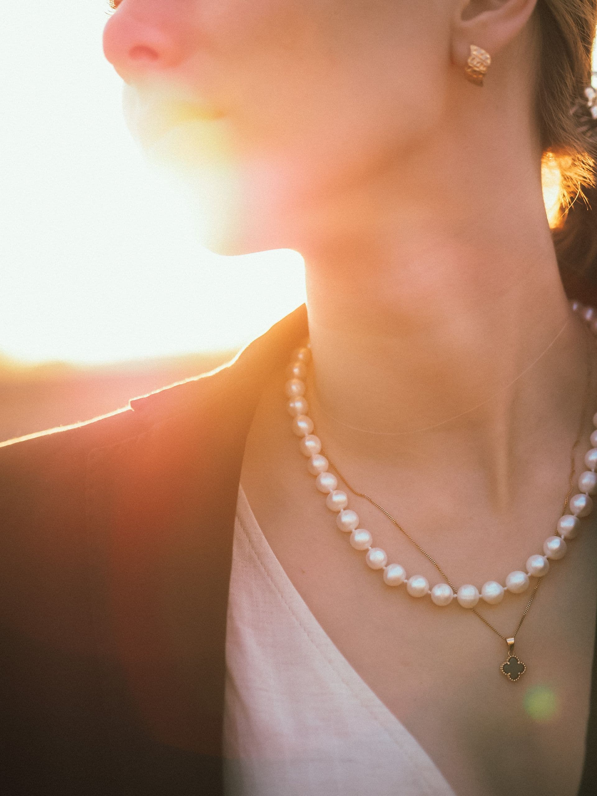 A woman wearing layered pearl necklaces, lit by golden hour sunlight